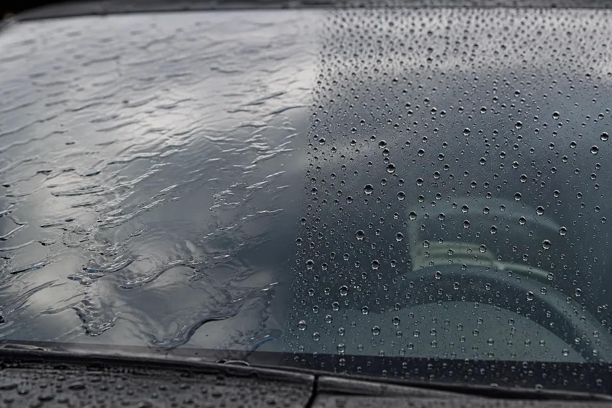 Gouttes d’eau perlant sur la moitié traitée d’un pare-brise sous la pluie
